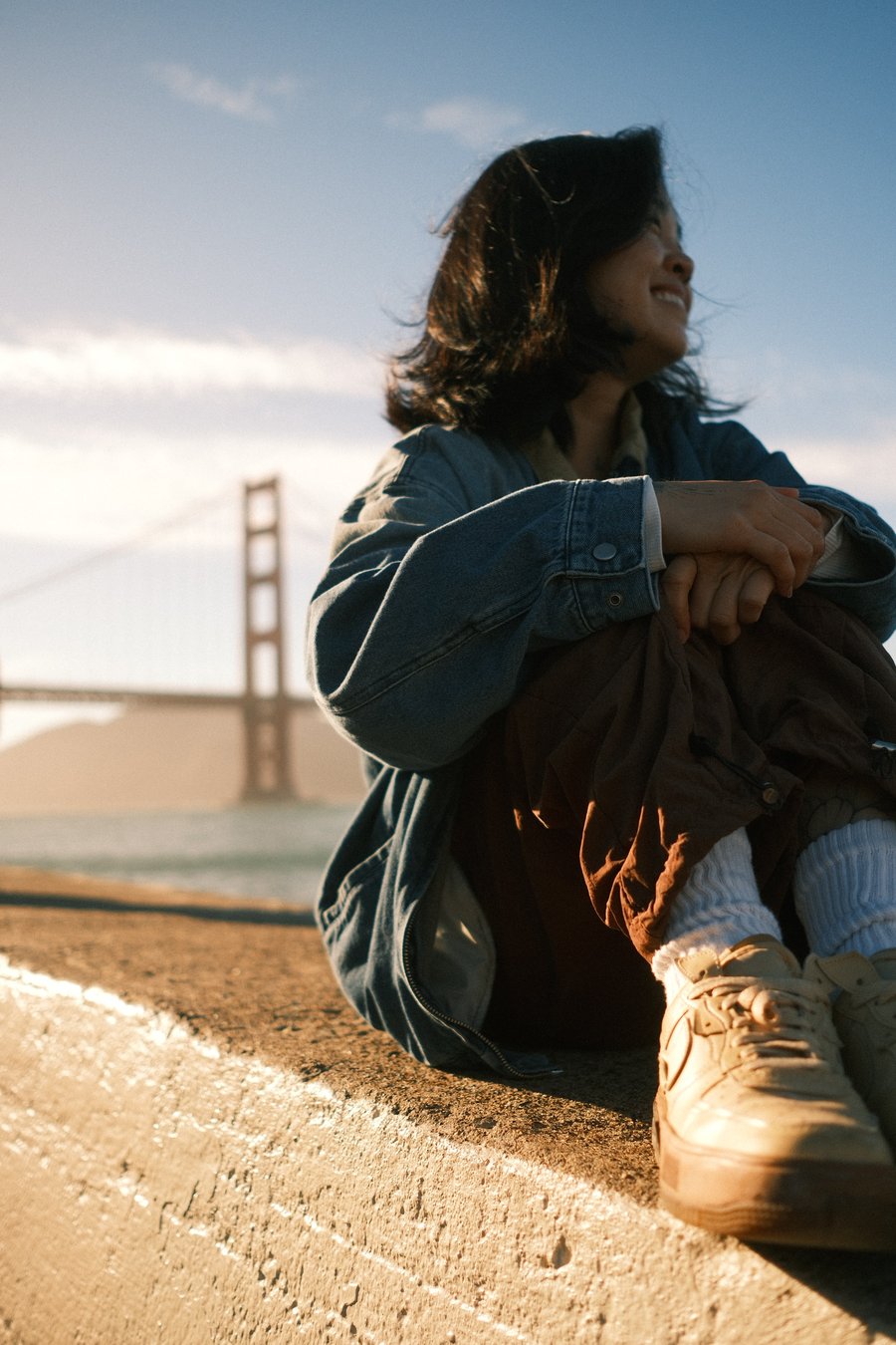 Susan Shao smiling and looking out at the Golden Gate Bridge, wearing a denim jacket.